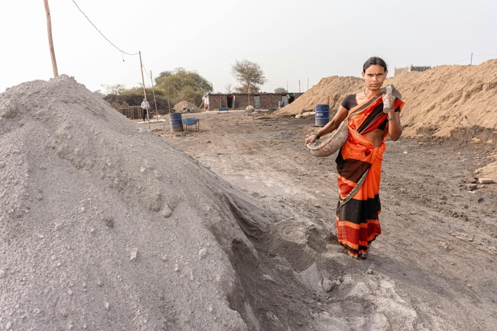 A woman in traditional attire carries material at an outdoor construction site in rural India.